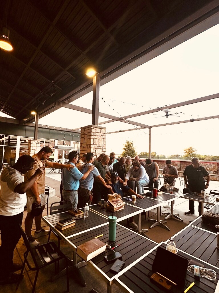 Godly Men gathered around tables praying together with hands on each other's shoulders